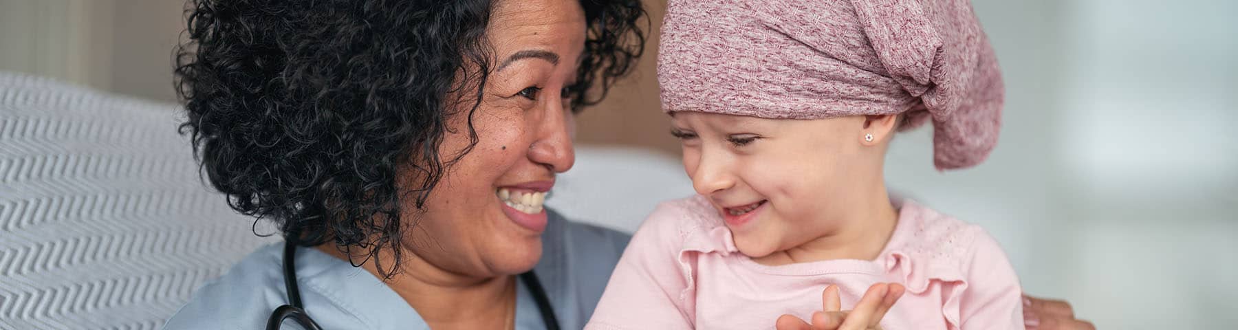 A nurse holding a young child who has cancer smiling together.