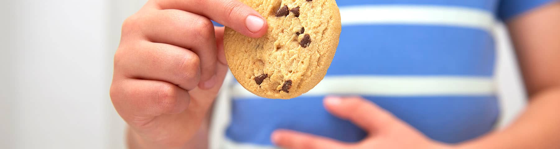 A child holding his stomach with one hand a cookie in the other hand.