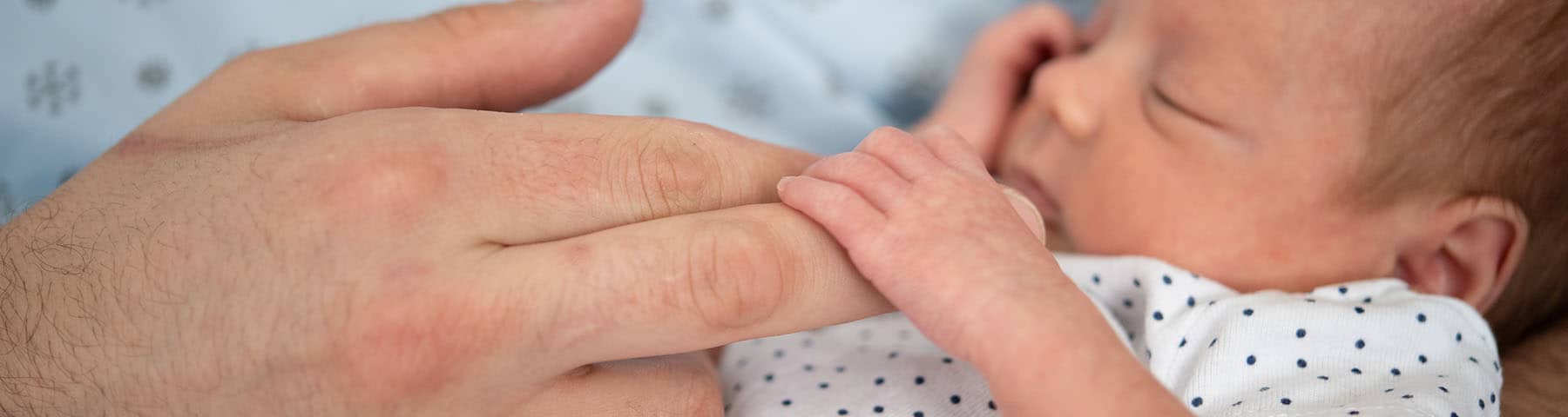 An infant baby holding and adult‘s finger.