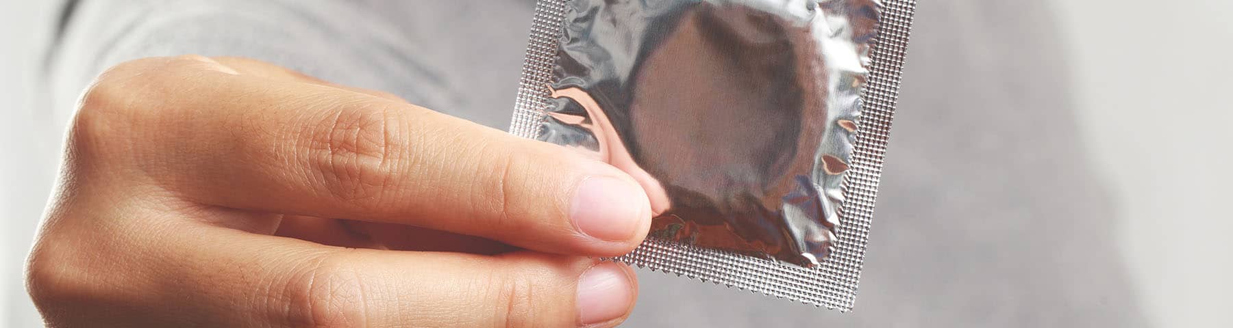 Close-up of a hand holding a sealed condom packet.