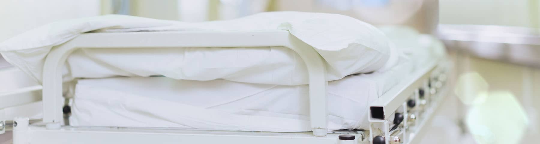 Empty hospital bed with white sheets in a clean medical facility.