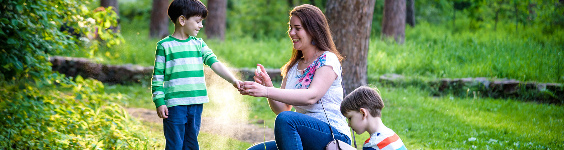 Mother applying bug spray to her child outdoors in a park.