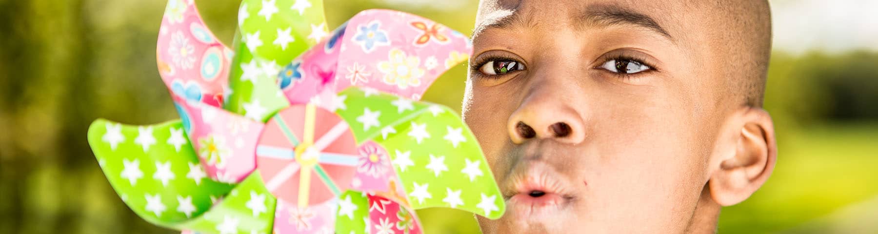 Child joyfully blowing on a colorful pinwheel in a sunny outdoor setting, evoking a sense of playfulness and hope.