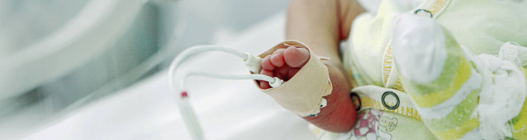 Close-up of a newborn's foot with medical monitoring equipment in a NICU setting.