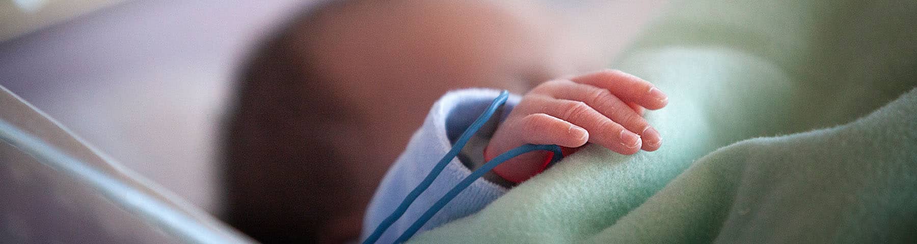 Close-up of a newborn's hand resting on a green blanket in a neonatal care setting.