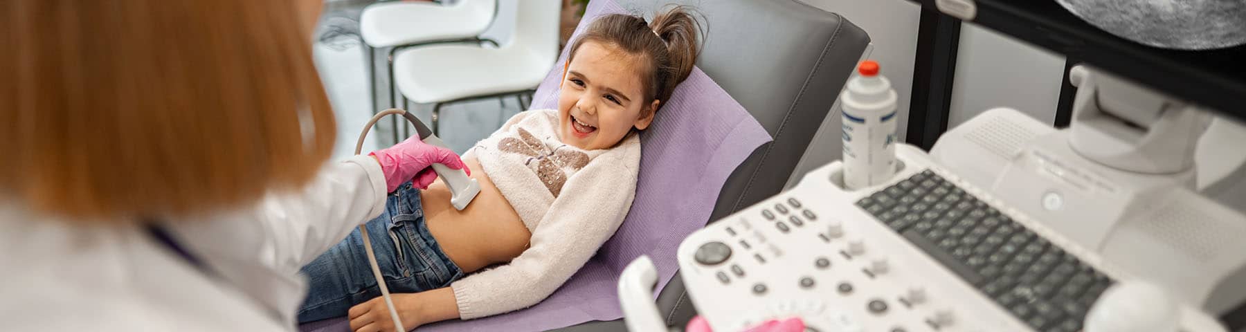 Smiling child undergoing an abdominal ultrasound exam in a medical clinic.