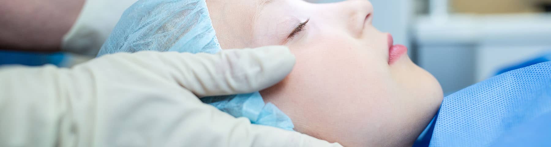 Child in a surgical cap being prepared for a procedure by a gloved medical professional.