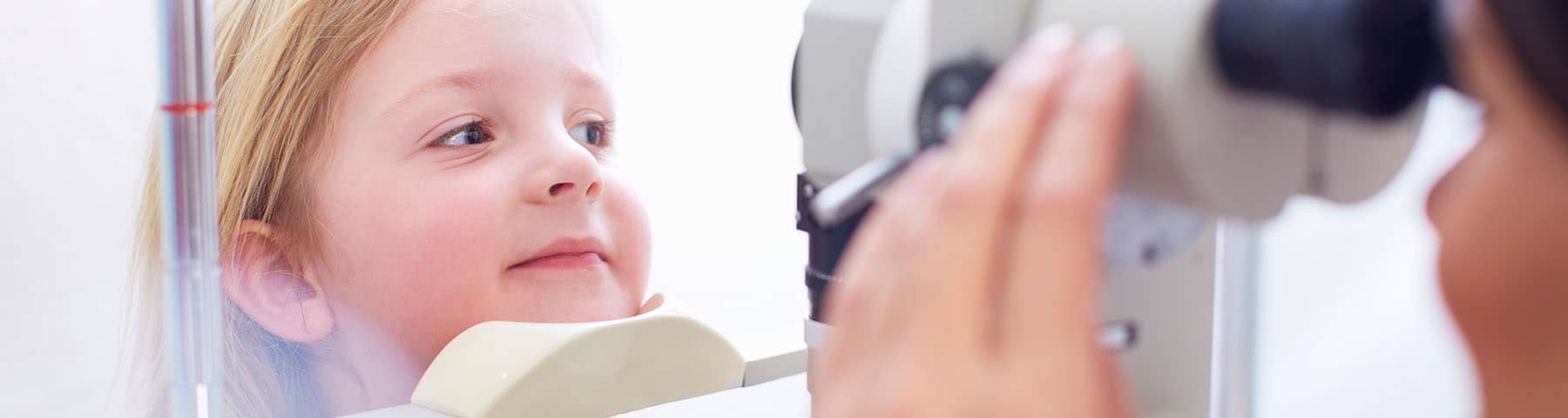 Young child undergoing an eye examination with a slit lamp in a clinic.