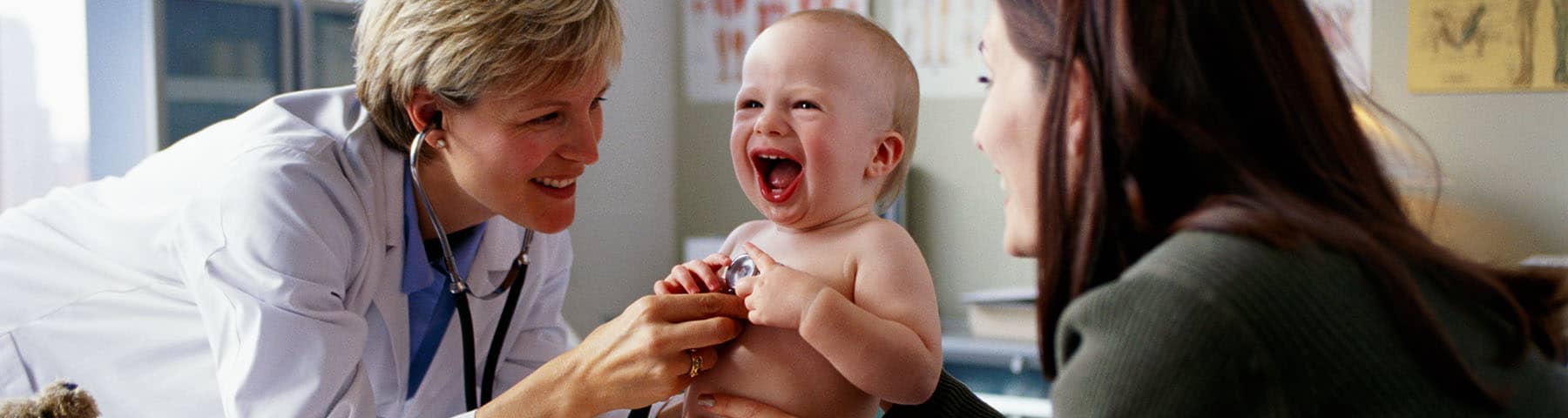 Happy baby laughing during a checkup with a doctor and a parent in a clinic.