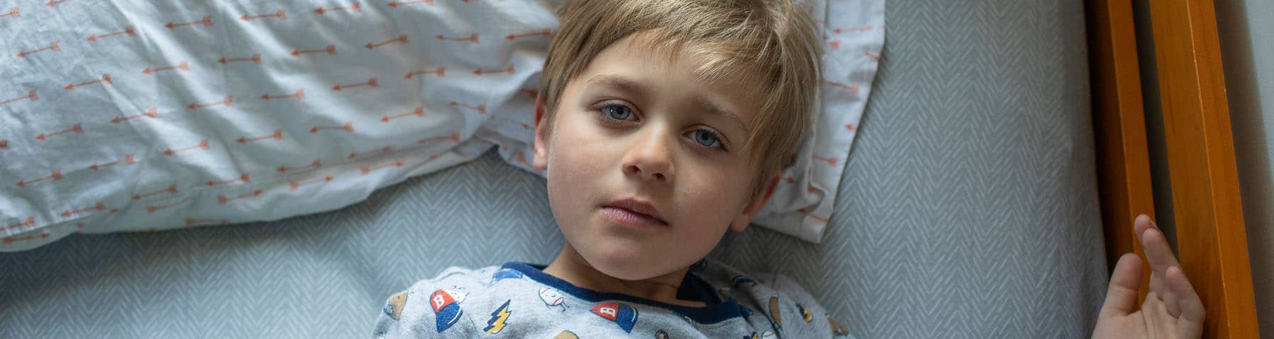 Child lying in bed, appearing thoughtful and awake.