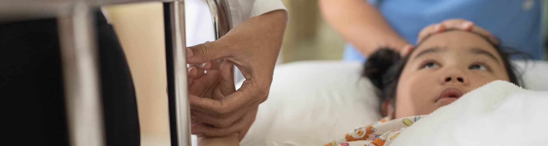 Child lying in a hospital bed being comforted by medical staff during treatment.