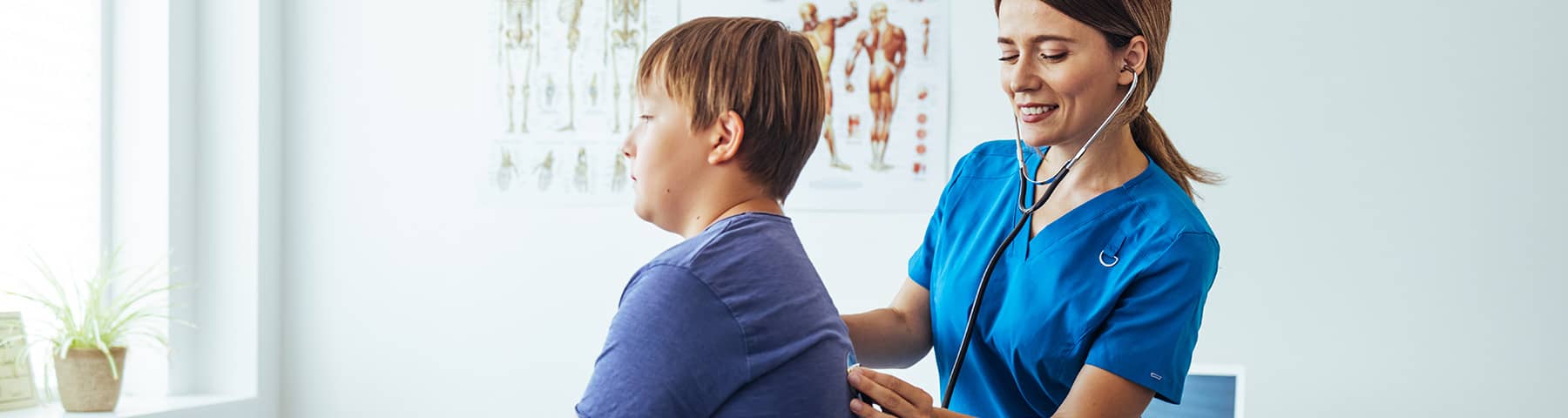 Nurse checking a young boy‘s breathing with a stethoscope on his back.