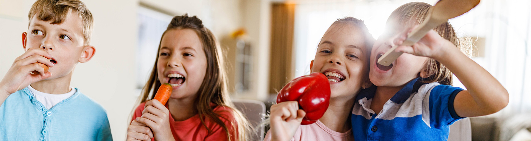 Group of children playfully pretending to eat vegetables and kitchen utensils.