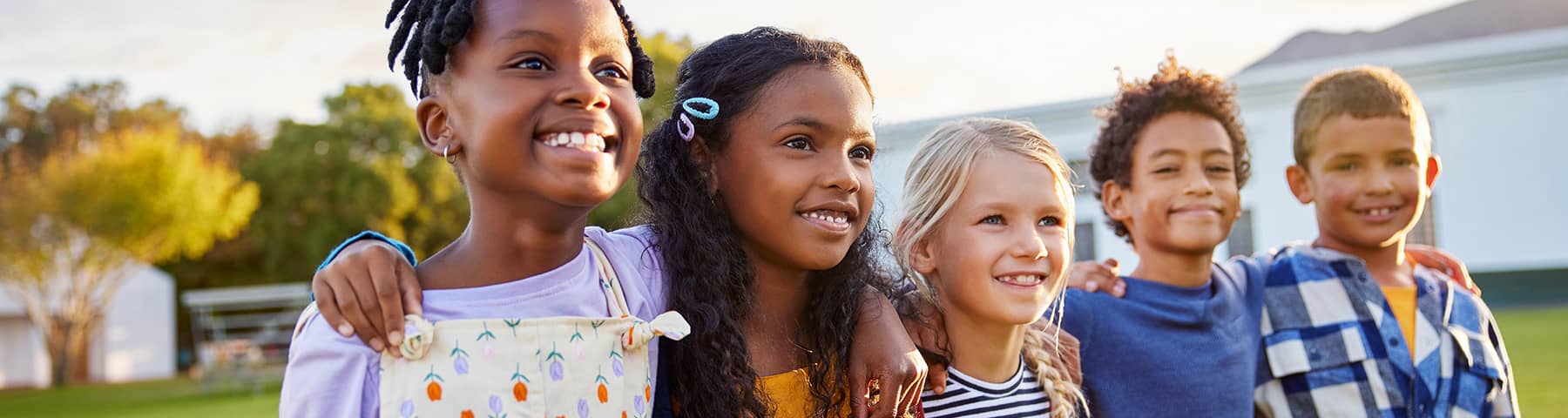 Group of smiling children standing outdoors with their arms around each other.