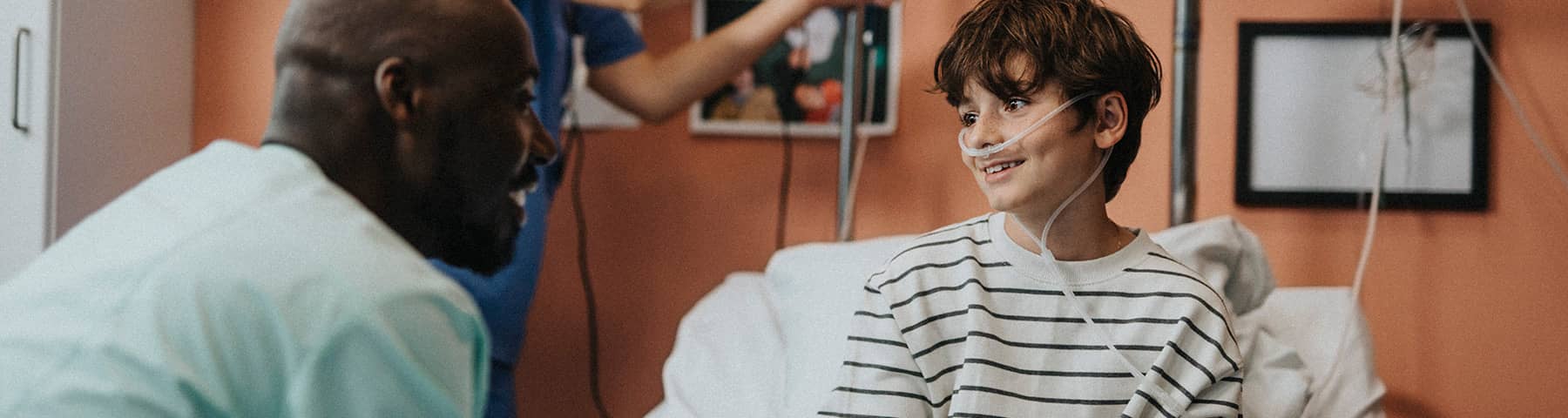 A young boy smiling and interacting with medical staff while sitting up on his hospital bed..