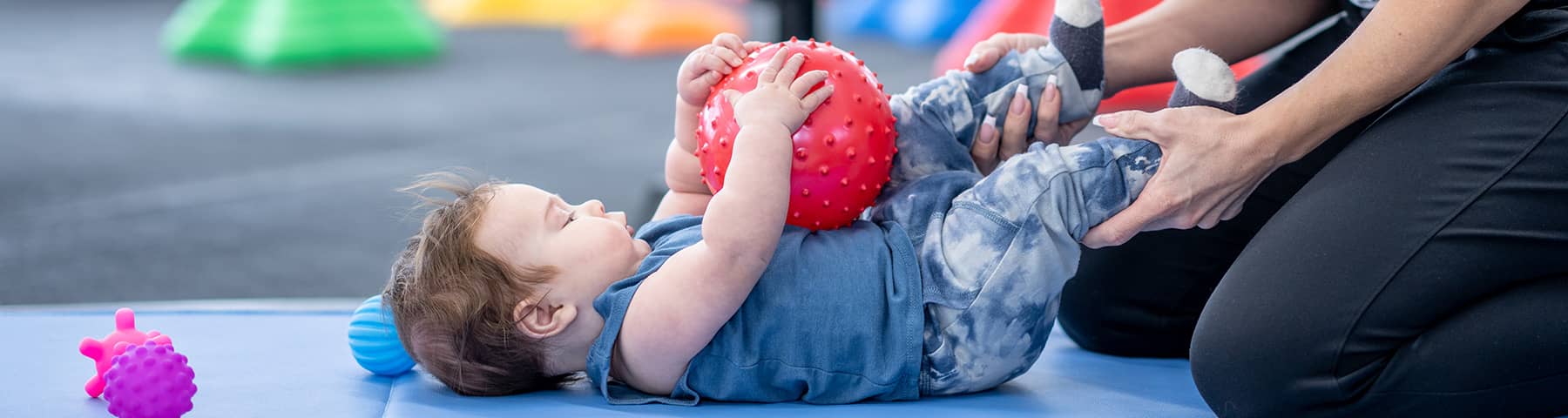 An infant laying down playing with a red ball.