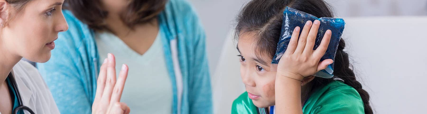 A young girl with an ice pack on her head, while the doctor is holding up three fingers to check for signs of concussion.