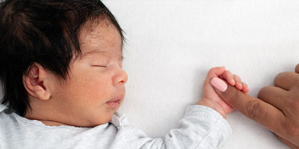 Infant baby sleeping on back with mom's index finger in the baby's palm.