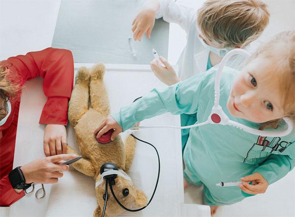 Children pretending to be doctors, examining a teddy bear with medical toys.